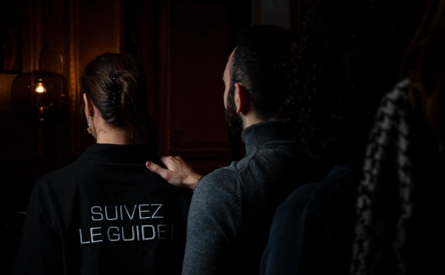 Personnes guidées dans l’obscurité lors d’une expérience immersive Dans le Noir ?, avec une guide portant l’inscription « Suivez le guide ».