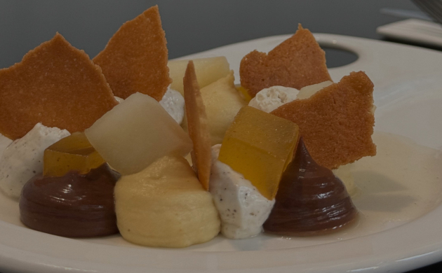 Photo du dessert de printemps avec des crèmes, des gelées de fruits, des morceaux de fruits frais et des tuiles croustillantes sur une assiette blanche.